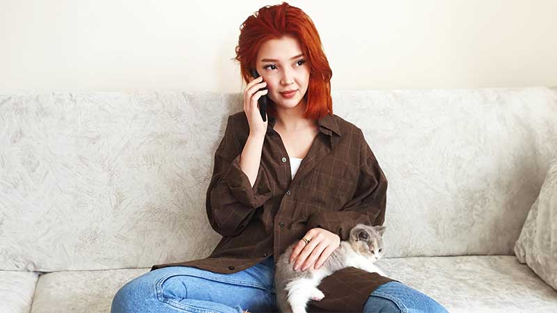 Rapariga a falar ao telemóvel sentada no sofá com um gato no colo